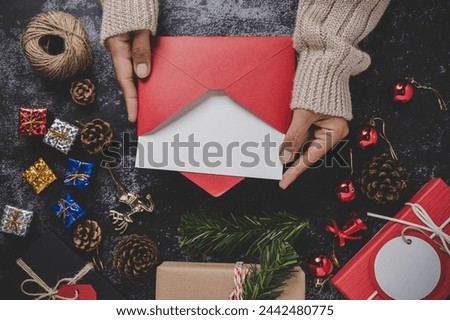 Hands holding opened card or letter. Blank cover Mock-up. With ribbons, gift boxes and dried pine cones on black background.