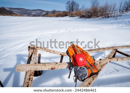 Red First Aid Kit Lying On Hiking Backpack On Snow Background, Hiking Gear, Orange Backpack, Winter Landscape. High quality photo
