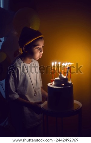 portrait boy in a yellow hat and white T-shirt blows out candles from a cake with a goose in the dark