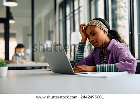 Pensive African American university student using laptop while learning in the classroom. Copy space.