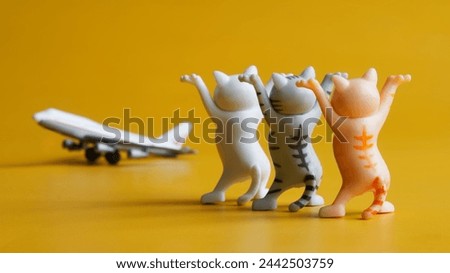Three toy kittens with raised paws and passenger airplane on yellow background. Concept of seeing off an airplane flight and air passengers. Happy flight. Toy world. Photo. Close-up
