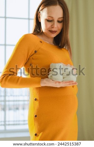 Pregnancy motherhood people expectation future. Pregnant woman with big belly holding newborn baby booties smiling at home. Young mom enjoying pregnancy. Maternity tenderness parenthood new life Royalty-Free Stock Photo #2442515387