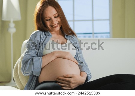 Pregnancy motherhood people expectation future. Pregnant woman touching big belly sitting on couch at home. Girl hugging her tummy enjoying pregnancy. Maternity tenderness parenthood new life concept Royalty-Free Stock Photo #2442515389