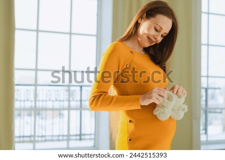 Pregnancy motherhood people expectation future. Pregnant woman with big belly holding newborn baby booties smiling at home. Young mom enjoying pregnancy. Maternity tenderness parenthood new life Royalty-Free Stock Photo #2442515393