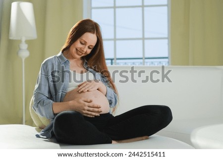 Pregnancy motherhood people expectation future. Pregnant woman touching big belly sitting on couch at home. Girl hugging her tummy enjoying pregnancy. Maternity tenderness parenthood new life concept Royalty-Free Stock Photo #2442515411
