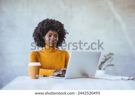 Positive woman video calling using laptop. Businesswoman teleconferencing on laptop while working. Modern Office: Black Businesswoman Sitting at Her Desk Working on a Laptop Computer.