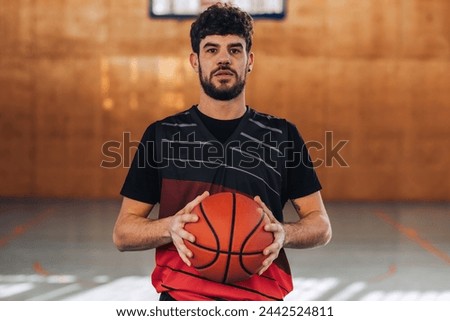 Portrait of a muscular basketball player standing on court with a basketball in his hands and looking at the camera. A professional masculine dedicated sportsman with ball in hands posing on court.