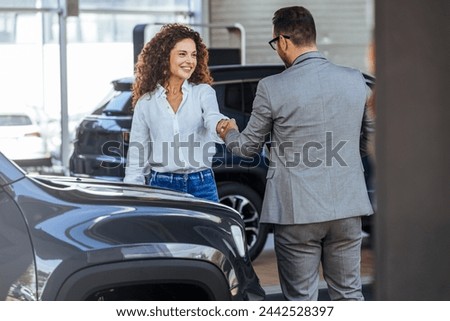Happy salesman congratulating his female customer for buying a new car in a showroom. Salesperson selling cars at car dealership.