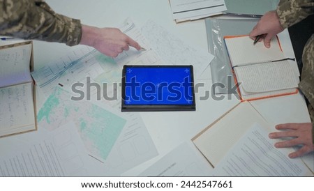 Group of security squad in control center. Military headquarters surveillance officers working in office at the table, tablet with blue screen, top view. Royalty-Free Stock Photo #2442547661