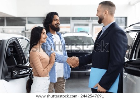 Young indian couple shaking hands with a car salesman in a dealership showroom, symbolizing a new car purchase Royalty-Free Stock Photo #2442547691