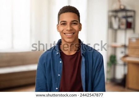 A cheerful young man in a casual shirt and jacket poses with a bright smile in a cozy home environment Royalty-Free Stock Photo #2442547877