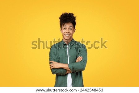 Amiable young black man with arms crossed, flashing a charming smile in front of a sunny yellow background Royalty-Free Stock Photo #2442548453