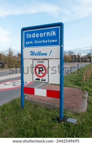 Place name sign for the village of Indoornik, municipality of Overbetuwe, the Netherlands, with the text 'welcome' below (and no parking for trucks or buses in this zone)