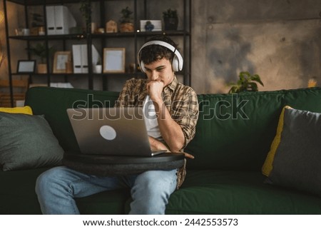 one yong man caucasian male teenager sit at home with headphones watch online movie video or series on laptop
