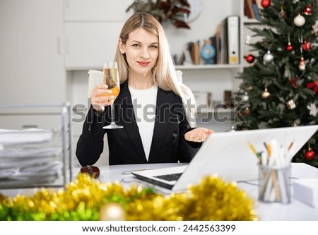 Business woman with a glass of champagne congratulates Merry Christmas on the Internet in the office