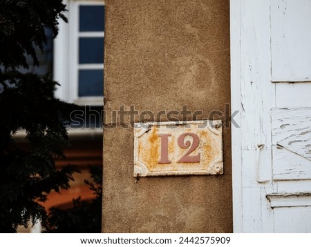 A house 12 twelve number sign is affixed to the side of a building, indicating the address of the property in a clear and prominently displayed manner