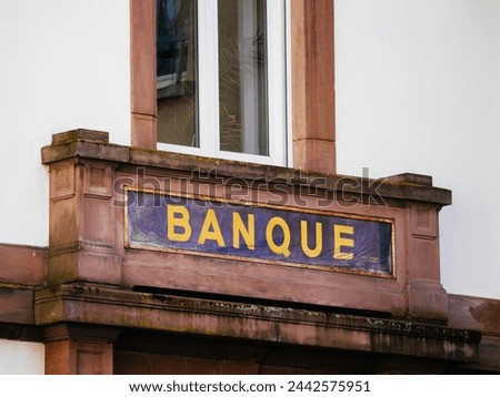 A classy Banque Bank sign displaying intricate details and elegant typography on the side of a weathered brick building in the city.