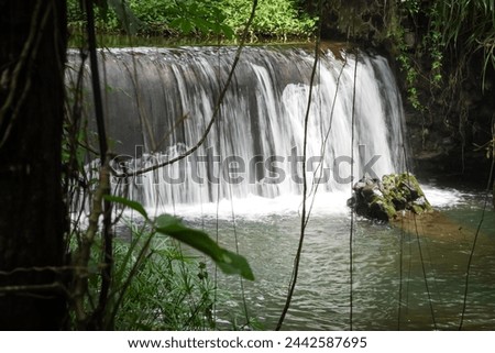 Long exposure photography - Dam on a rocky river with clear water natural pool surrounded by trees and vines. Artificial Waterfall in Sleman, Yogyakarta, Indonesia. Concept for environment