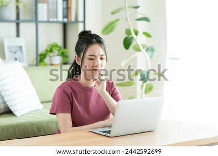 A Japanese woman worries while using a computer in the living room.