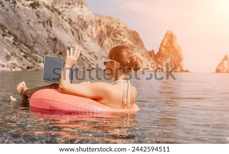 Woman freelancer works on laptop swimming in sea on pink inflatable ring. Happy tourist in sunglasses floating on inflatable donut and working on laptop computer in calm ocean. Remote working anywhere