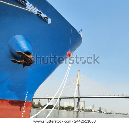 Anchor with large cargo ship's, anchor being pulled. Blue and red ship, While docked at the pier by large ropes on the river, isolated on high brigde with blue sky background  and transport concept