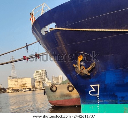 Anchor on large cargo ship's, anchor being pulled. Blue and green ship, While docked at the pier by large ropes on the river, isolated on the buildings with blue sky background and transport concept