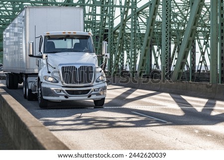 Industrial carrier local hauler white day cab big rig semi truck tractor transporting cargo in dry van semi trailer running on the arched truss I-5 Interstate Bridge Royalty-Free Stock Photo #2442620039