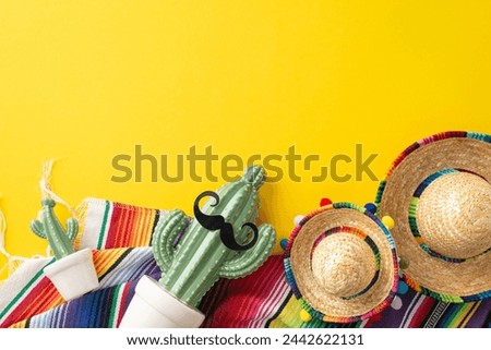 Cinco de Mayo collection. Overhead view of symbolic pieces: little sombreros, a decorated cactus, a patterned serape, arranged on a sunlit yellow background Royalty-Free Stock Photo #2442622131