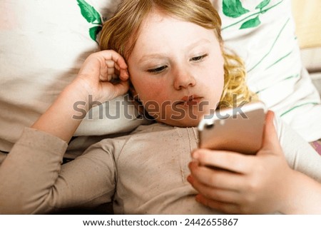 A young girl is lying in bed and using a mobile phone.