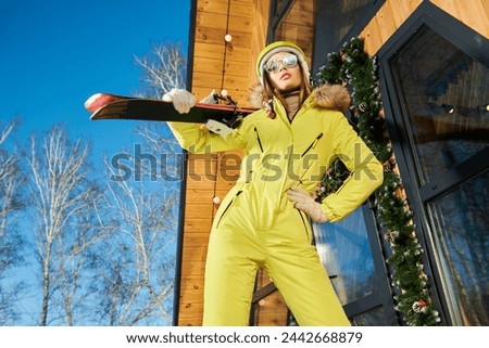 A happy girl in a down ski-suit stands  at a ski resort. Sunny winter day. Skiing and winter recreation.