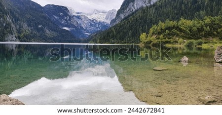 A view of a mountain lake in which the mountains and the sky are reflected. There is a forest all around. 
