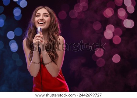 Beautiful woman with microphone singing on stage in color lighted smoke Royalty-Free Stock Photo #2442699727