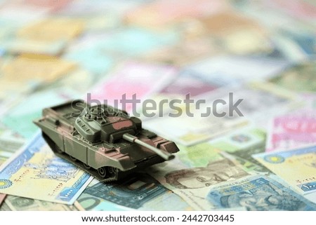 Small green tank on many banknotes of different currency. Background of war funding or spend money to defense close up Royalty-Free Stock Photo #2442703445