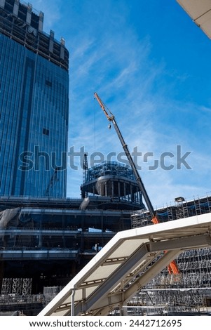 Mobile crane at construction site with glass facade of modern office tower at Takanawa district of Japanese metropolis of Tokyo on a sunny winter day. Photo taken  February 16th, 2024, Tokyo, Japan.