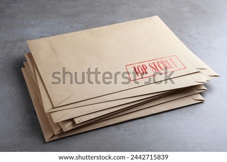 Top Secret stamp. Stacked paper envelopes on grey table