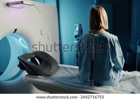 Rear view shot of unrecognizable woman wearing patient gown sitting on modern CT scanner bed, copy space Royalty-Free Stock Photo #2442716753