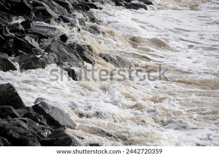 Waves crash on granite stones during a storm on the Black Sea coast. City embankment on a cloudy winter day.