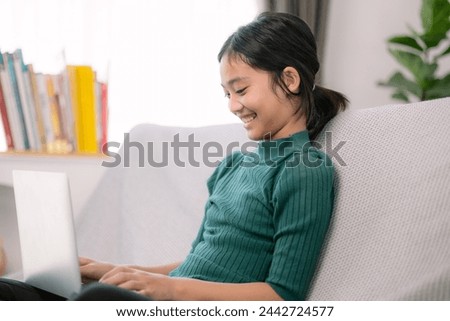 Asian young girls doing homework on laptops on a comfortable couch.