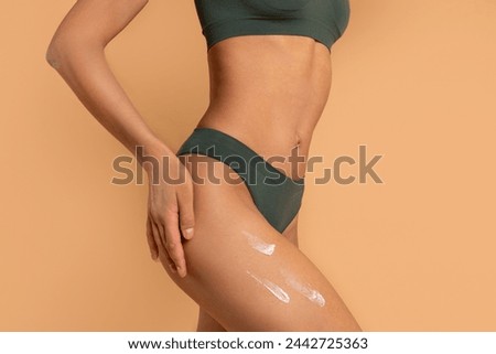 Slim woman in panties applying moisturising body cream on her legs, using anti-cellulite lotion or sunscreen, closeup
