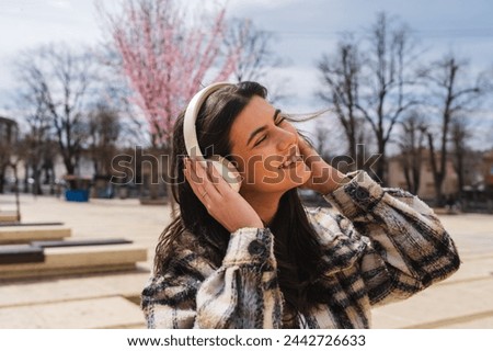One young girl or woman is listening to music on her wireless headphones and enjoying the sun outdoors	
