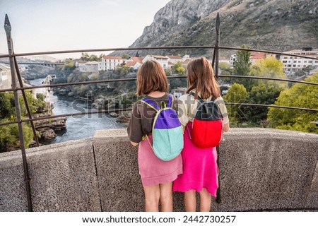 Twin girls standing on famous Mostar bridge, looking at Mostar town and river Neretva in Bosnia and Herzegovina. Historical Mostar Bridge known also as Stari Most or Old Bridge in Mostar. Royalty-Free Stock Photo #2442730257