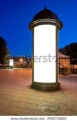 Blank Mockup Of Round Billboard In A City Square At Night. Classic Style Column Lightbox In The Old Town