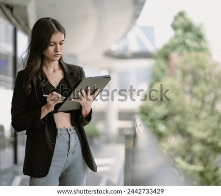 Confident businesswoman using digital tablet while standing outside office. Long hair beautiful business woman working outdoor checking information online. Success female CEO entrepreneur in suit.