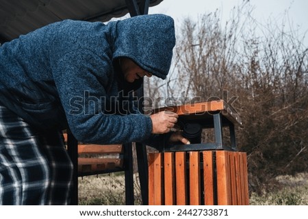homeless elderly old Caucasian man rummages for food and garbage in a trash can in a park in autumn Royalty-Free Stock Photo #2442733871