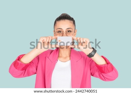 Holding credit card, young rich brunette caucasian woman 20s holding credit card. Wear pink jacket. Cover her face. Light blue background. People lifestyle. Pay, payment, moneyless concept idea.