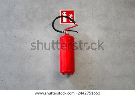 Red fire extinguisher hanging on gray concrete wall. Emergency equipment. Industrial building space. Royalty-Free Stock Photo #2442751663