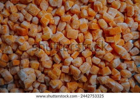 Dense arrangement of frozen pumpkin cubes covered with frost, displaying a bright orange hue.