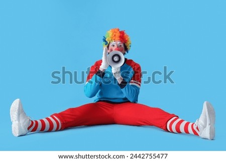 Portrait of clown with megaphone sitting on blue background. April Fool's day celebration