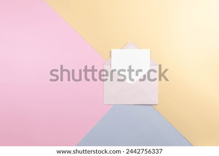 Top view of pink envelope and white card on colourful background. Blue, pink and yellow background. Colourful wallpaper, copy space.