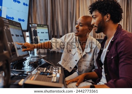 Creative professionals are engaged in a focused discussion at a music production studio. The image captures a moment of collaboration, with modern recording equipment and computers in the background.